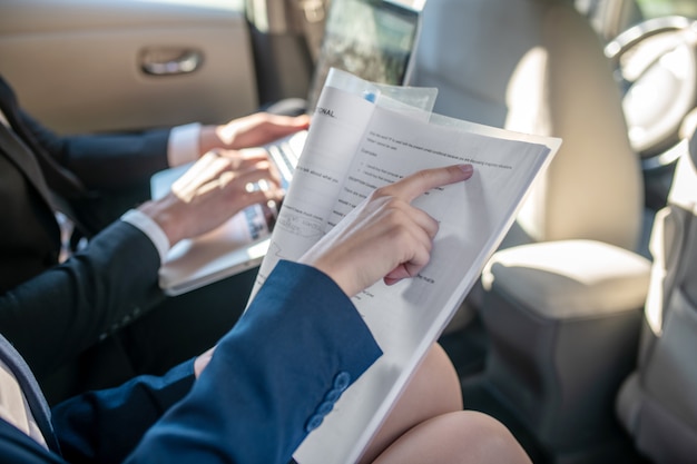 Mains féminines tenant un document, mens sur clavier d'ordinateur portable