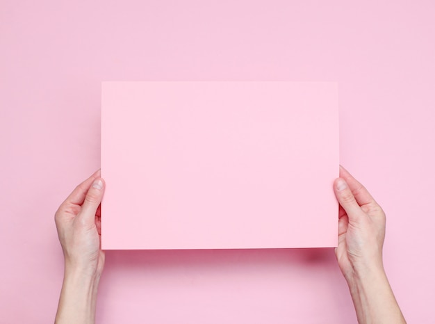 Mains féminines tenant une feuille de papier rose sur rose