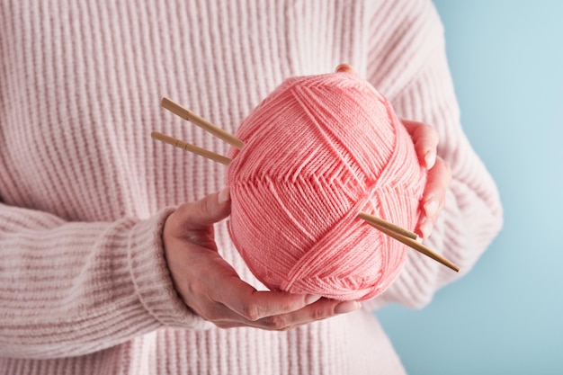 Mains féminines tenant des fils de laine roses colorés et des aiguilles à tricoter en bois pour passe-temps ou travail d'art sur fond bleu Couture ou concept de tricot Image en gros plan