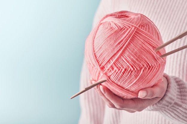 Mains féminines tenant des fils de laine roses colorés et des aiguilles à tricoter en bois pour passe-temps ou travail d'art sur fond bleu Couture ou concept de tricot Image en gros plan