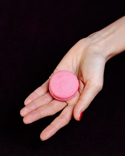 Photo des mains féminines tenant des macarons sur un fond sombre concept sucré minimaliste vue supérieure