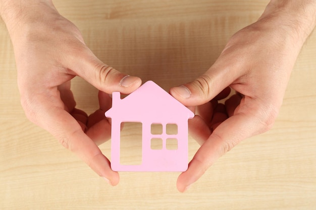 Mains féminines tenant maison sur fond de bois