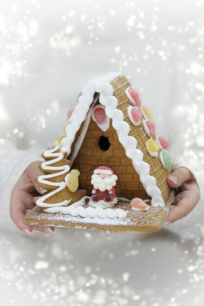 Mains féminines tenant une maison de pain d'épice festive avec de la neige