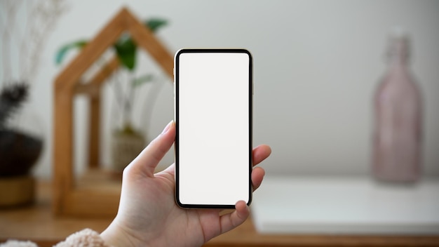 Mains féminines tenant une maquette d'écran blanc de smartphone sur fond de salon minimal flou