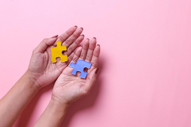 Mains féminines tenant des pièces de puzzle colorées sur fond de couleur rose Journée mondiale de sensibilisation à l'autisme