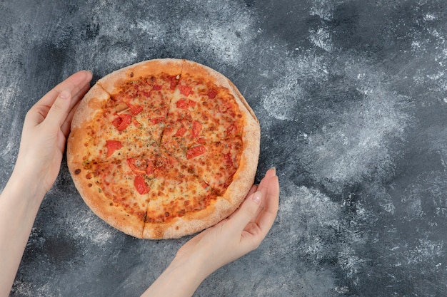 Mains féminines tenant une pizza entière fraîche sur une surface en marbre. Illustration 3d de haute qualité