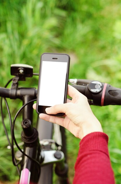 Mains féminines tenant un smartphone assis sur un vélo de montagne sur une route forestière. Navigation de concept, sports actifs d'été, technologie.