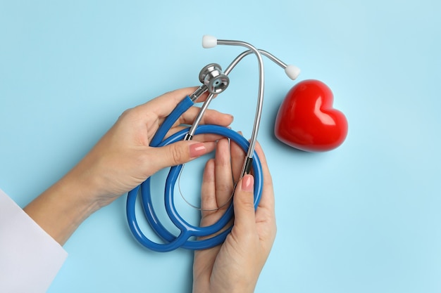 Mains féminines tenant stéthoscope sur bleu avec coeur