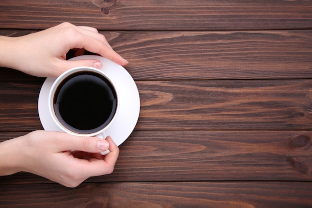 Mains féminines tenant la tasse de café en bois marron.