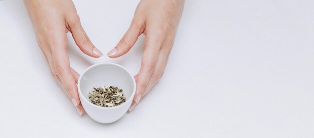 Mains féminines tenant une tasse avec des extraits de plantes sèches biologiques pour une tisane purifiante