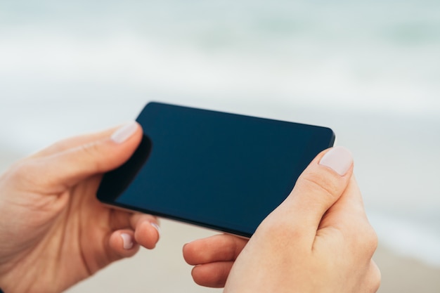 Mains féminines tenant le téléphone avec écran tactile sur le fond de la mer