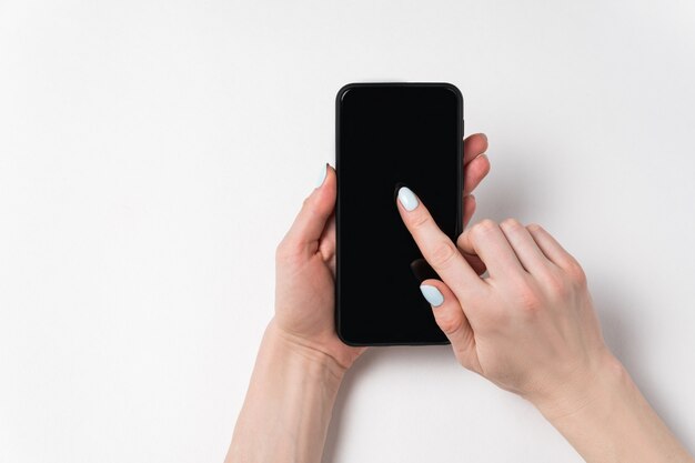 Mains féminines tenant le téléphone et montrant à l'écran. Affichage noir, fond blanc, espace copie