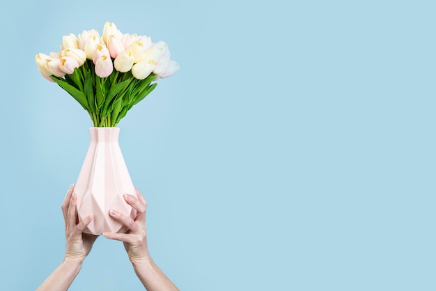 Photo mains féminines tenant un vase avec un bouquet de tulipes sur fond bleu