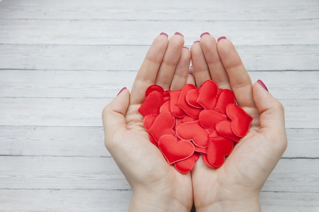 Des mains féminines tiennent beaucoup de coeurs rouges dans la paume sur un fond en bois, concept de sauver l&#39;amour