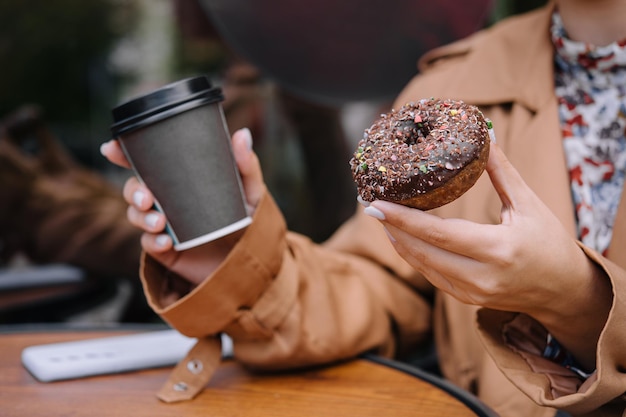 Les mains féminines tiennent un beignet et une tasse de café