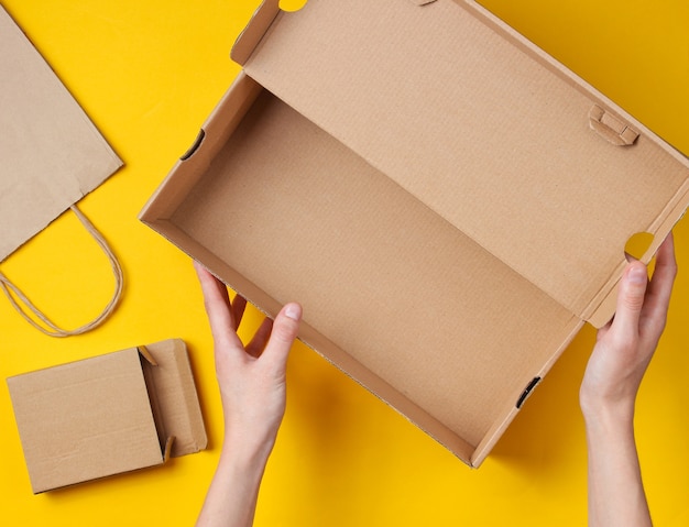 Les mains féminines tiennent une boîte en carton vide sur un jaune avec un sac en papier et une boîte. Vue de dessus