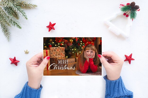 Des mains féminines tiennent une carte de voeux de Noël sur le fond d'une table blanche avec un décor de Noël.