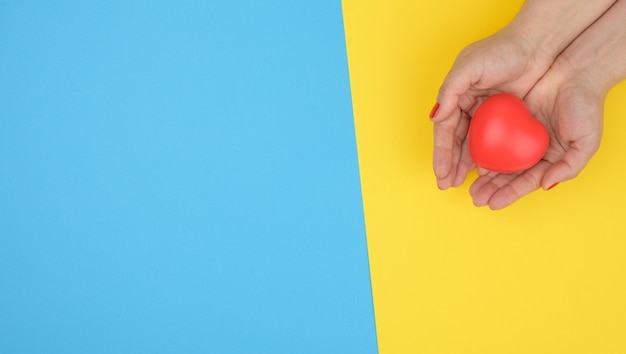 Les mains féminines tiennent le coeur rouge, fond bleu. Concept d'amour et de don, espace de copie