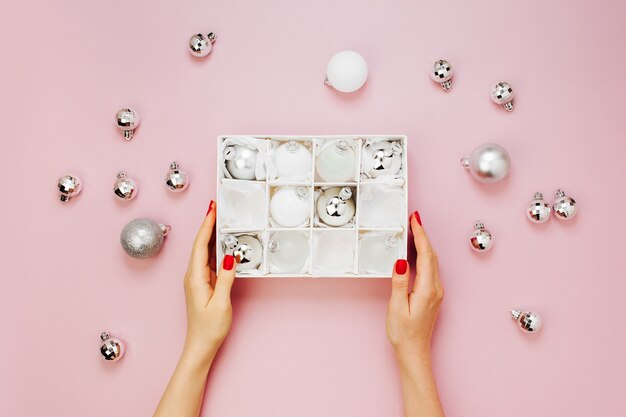 Les mains féminines tiennent un ensemble élégant de boules de Noël argentées brillantes. Concepts de vacances. Mise à plat, vue de dessus