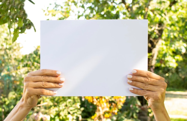 Les mains féminines tiennent une feuille de papier blanc vide sur le fond de la nature