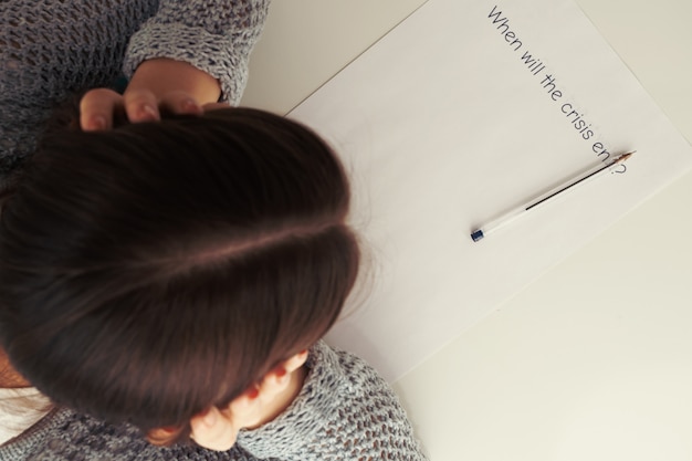 Des mains féminines tiennent leur tête sur une feuille de papier avec l'inscription à la fin de la crise