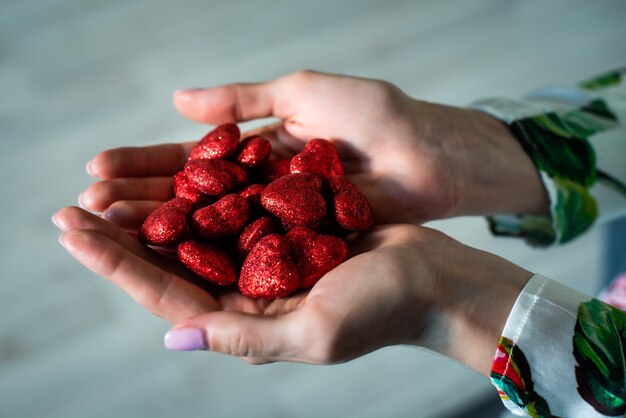 Les mains féminines tiennent de nombreux coeurs rouges brillants. La Saint-Valentin. Amour, 14 février. Le concept d'amour, de confiance, de foi, d'aide.