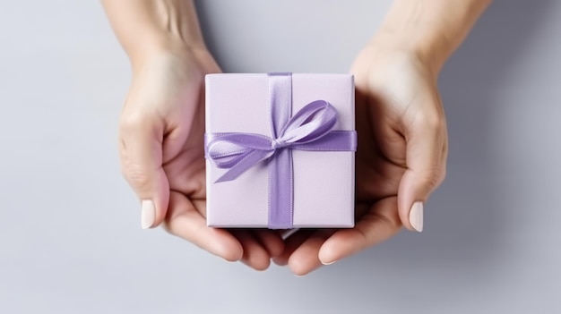 Des mains féminines tiennent une petite boîte à cadeaux sur une table blanche.