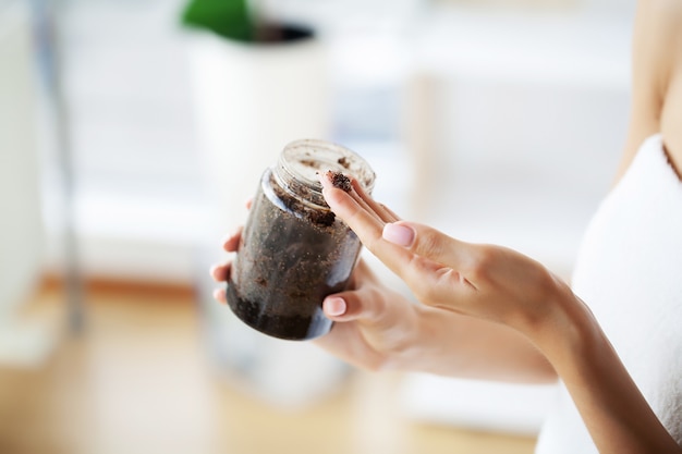 Des mains féminines tiennent un pot de gommage au café.