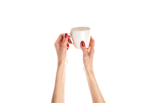 Mains féminines tiennent une tasse en céramique blanche sur fond blanc Mains féminines avec manucure rouge fraîche Isolé sur fond blanc