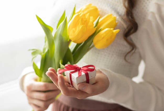 Des mains féminines tiennent des tulipes et une boîte-cadeau