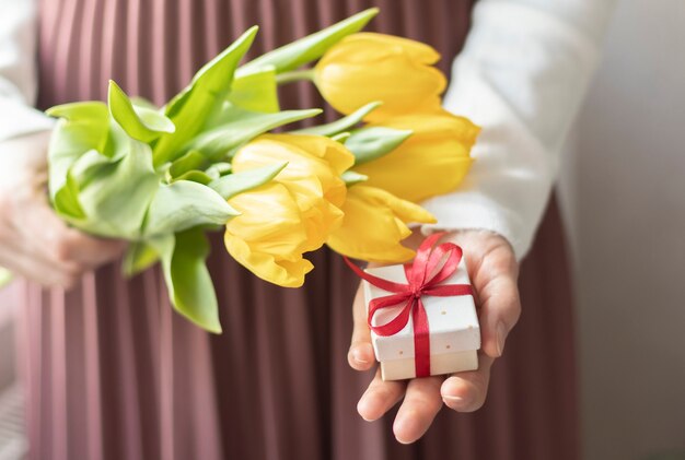 Des mains féminines tiennent des tulipes et une boîte-cadeau