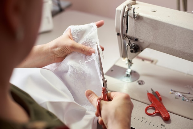 Photo mains féminines travaillant à l'aide de ciseaux pour couper le tissu dans le processus de couture vue rapprochée arrière-plan flou