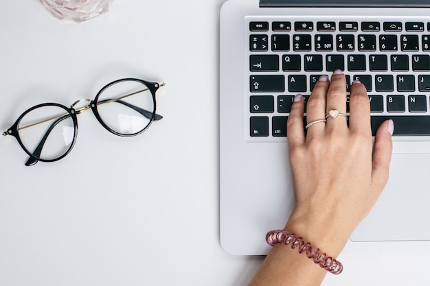 Des mains féminines utilisent un clavier d'ordinateur portable sur une table blanche