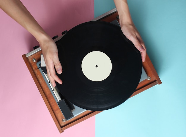 Les mains féminines utilisent un lecteur de vinyle rétro sur pastel rose bleu. DJ. Vue de dessus