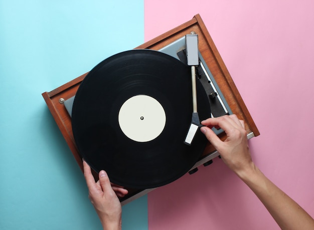 Les mains féminines utilisent un lecteur de vinyle rétro sur pastel rose bleu. DJ. Vue de dessus