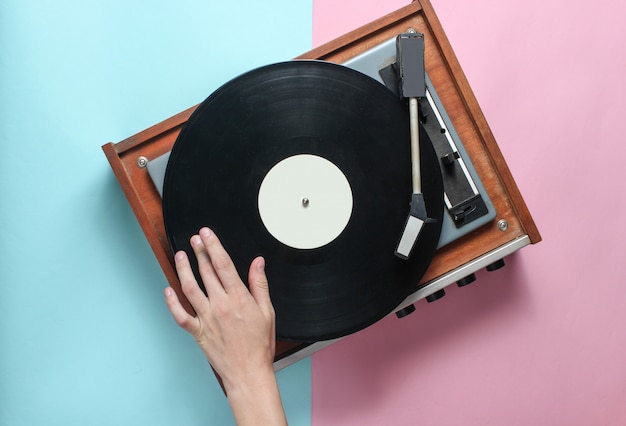 Les mains féminines utilisent un lecteur de vinyle rétro sur pastel rose bleu. DJ. Vue de dessus