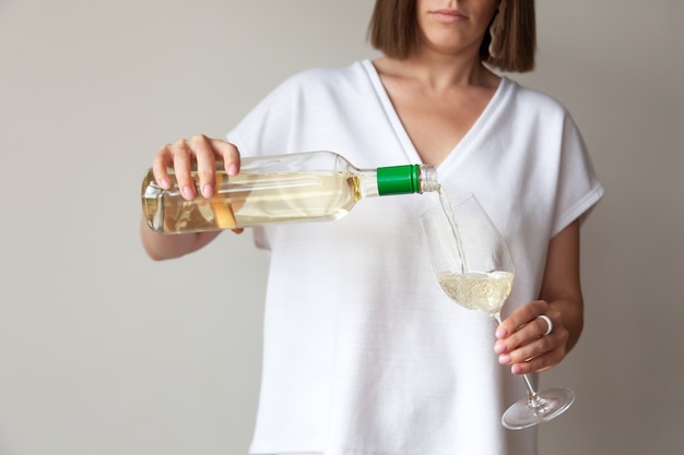 Des mains féminines versent du vin blanc de la bouteille au verre