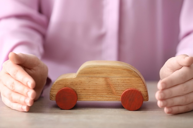 Mains féminines et voiture jouet en bois sur table Concept d'assurance voyage