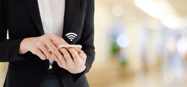 Mains de femme d&#39;affaires à l&#39;aide de téléphone intelligent avec l&#39;icône de wifi sur le bureau de flou avec la lumière de bokeh