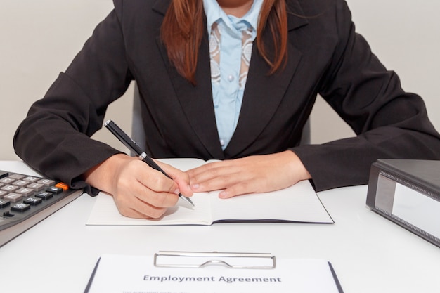 Mains de femme d&#39;affaires écrivant sur ordinateur portable avec calculatrice et contrat de travail