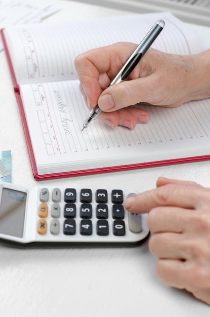 Les mains d'une femme âgée comptent les finances sur une calculatrice Le retraité calcule les coûts des services publics