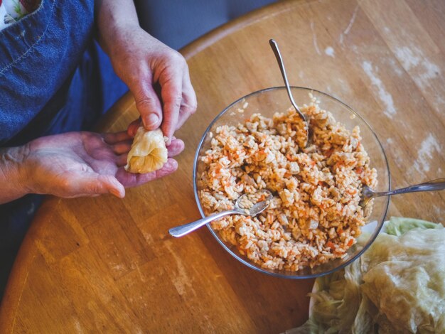 Mains d'une femme âgée enveloppant un chou farci de choucroute crue farci de riz et de viande