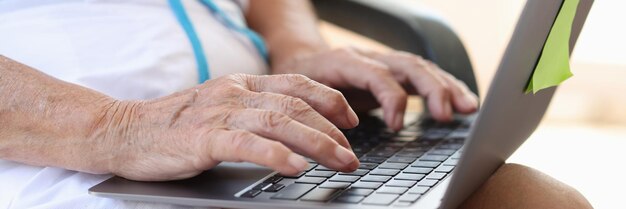 Les mains d'une femme âgée mature tapent sur un ordinateur portable à la recherche d'informations sur Internet et