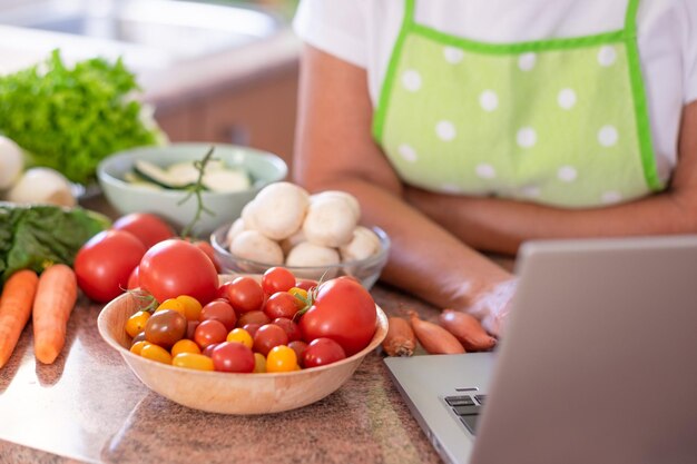 Les mains d'une femme âgée préparant des légumes dans la cuisine à domicile en recherchant de nouvelles recettes sur le Web à partir d'un ordinateur portable