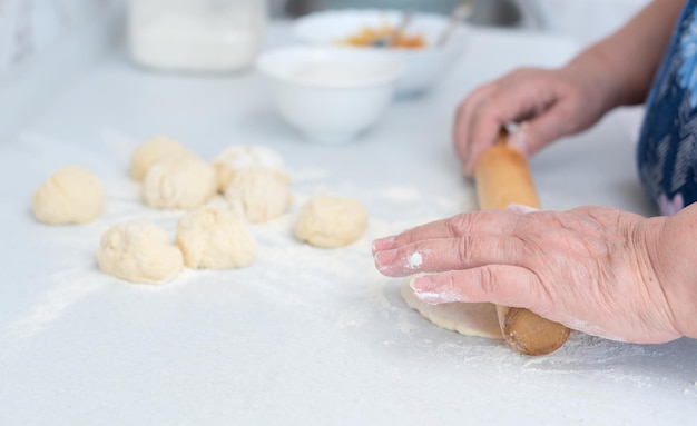 Mains de femme âgée roulant la pâte avec un rouleau à pâtisserie sur une table de cuisine blanche avec pomme râpée floue et sucre sur fond Mise au point sélective Processus de fabrication de tartes fourrées aux pommes