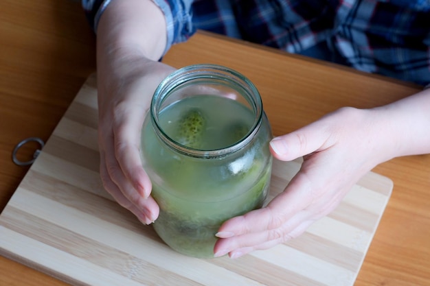 Les mains d'une femme âgée sortent de délicieux concombres marinés faits maison dans un pot pour les couper comme collation dans la cuisine sur une table brune sans gros plan du visage