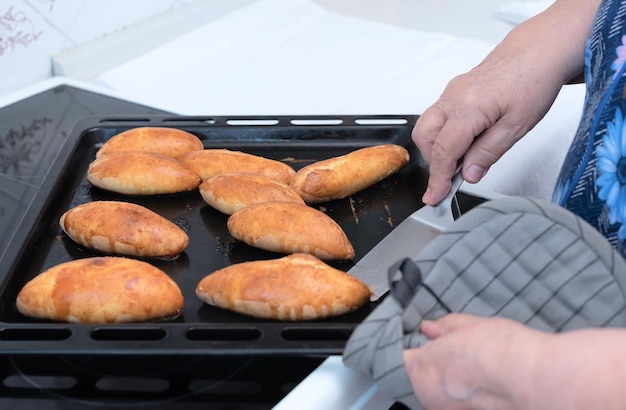 Les mains d'une femme âgée sortent des tartes prêtes à l'emploi avec une garniture aux pommes de la plaque de cuisson Mise au point sélective Processus de fabrication de tartes avec une garniture aux pommes Concept de cuisine à la maison Cuisine traditionnelle faite maison