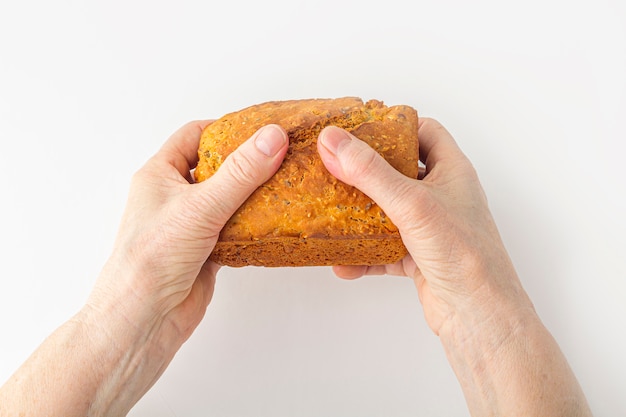 Les mains d'une femme âgée tiennent un petit pain de grains entiers fait maison fraîchement cuit sur une surface blanche. Concept de main secourable. Copiez l'espace pour le texte