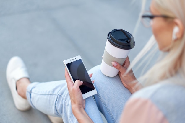 Mains de femme à l'aide de téléphone et tenant une tasse de papier avec du café