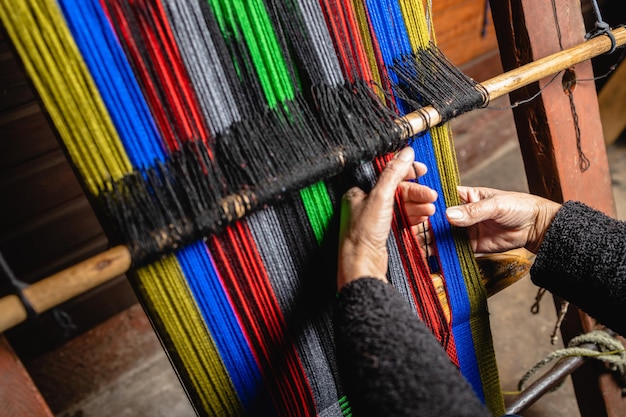 Les mains d'une femme aînée méconnaissable utilisant un métier à tisser artisanal pour tisser de la laine colorée